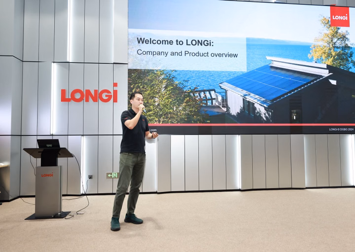 Man giving a presentation in front of a large screen displaying the LONGi logo and a house with solar panels.