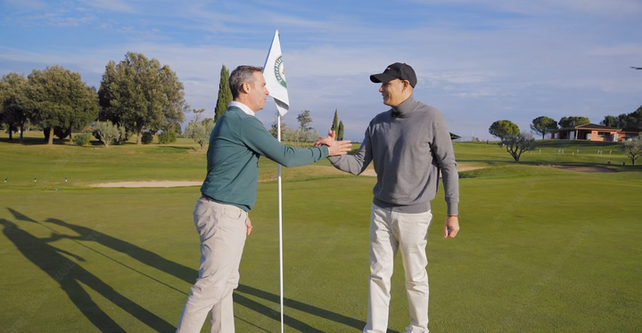 Two men shaking hands on a golf course near a flag, representing LONGi Solar and Torremirona Golf Club.