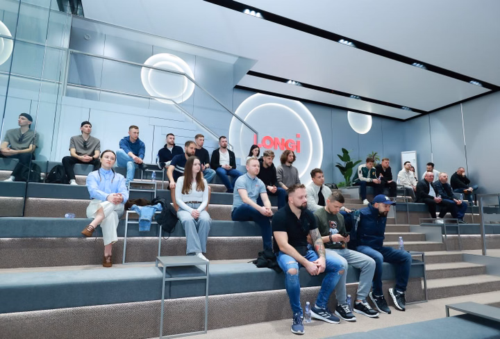 A group of people watch a presentation in a modern auditorium at the LONGi Lighthouse Factory.