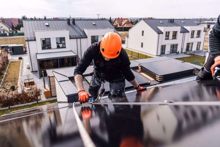 Worker in safety gear installing solar panels on a roof.