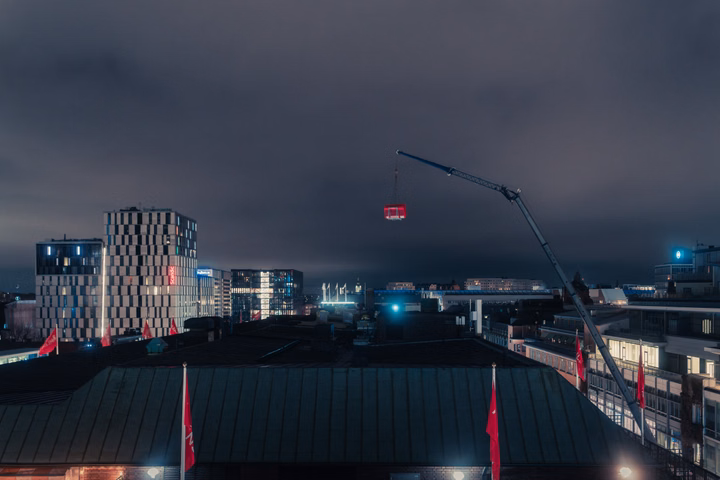 Crane lifting a red solar component over Stockholm buildings at night.