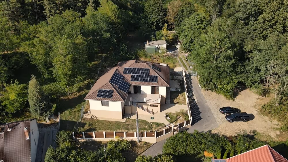 A modern house with solar panels on the roof, surrounded by trees.