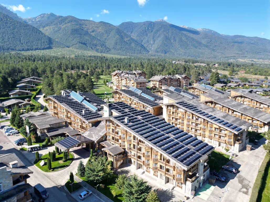 Aerial view of Pirin Golf and Spa resort featuring rooftop solar panels against a mountain backdrop.