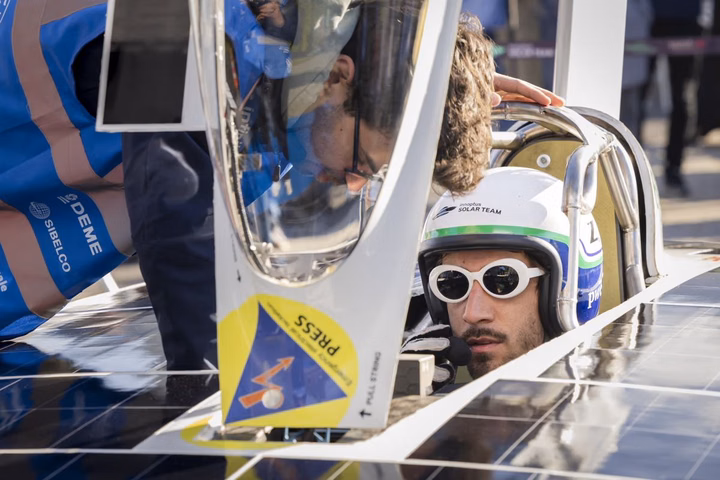A driver wearing sunglasses and a helmet sits in the Infinite Apollo solar race car during a road test.