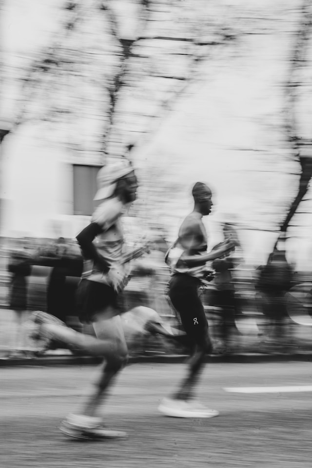 Motion-blurred black and white photo of two marathon runners racing past bare trees
