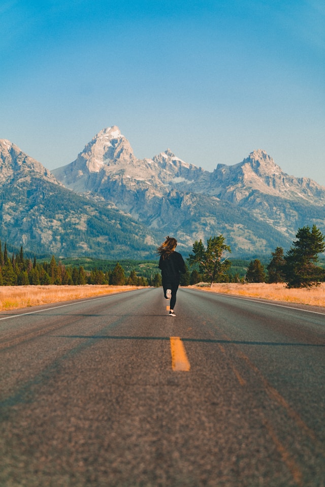 	Woman running down an open road toward snow-capped mountains