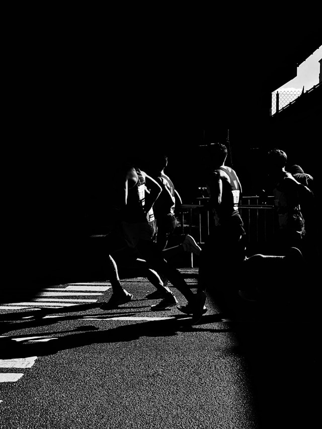 High-contrast black and white photo of runners crossing a shadowed street during a race