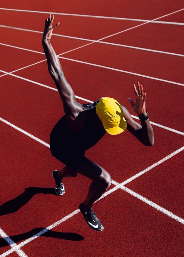 Sprinter exploding out of the blocks on a red running track, arms raised